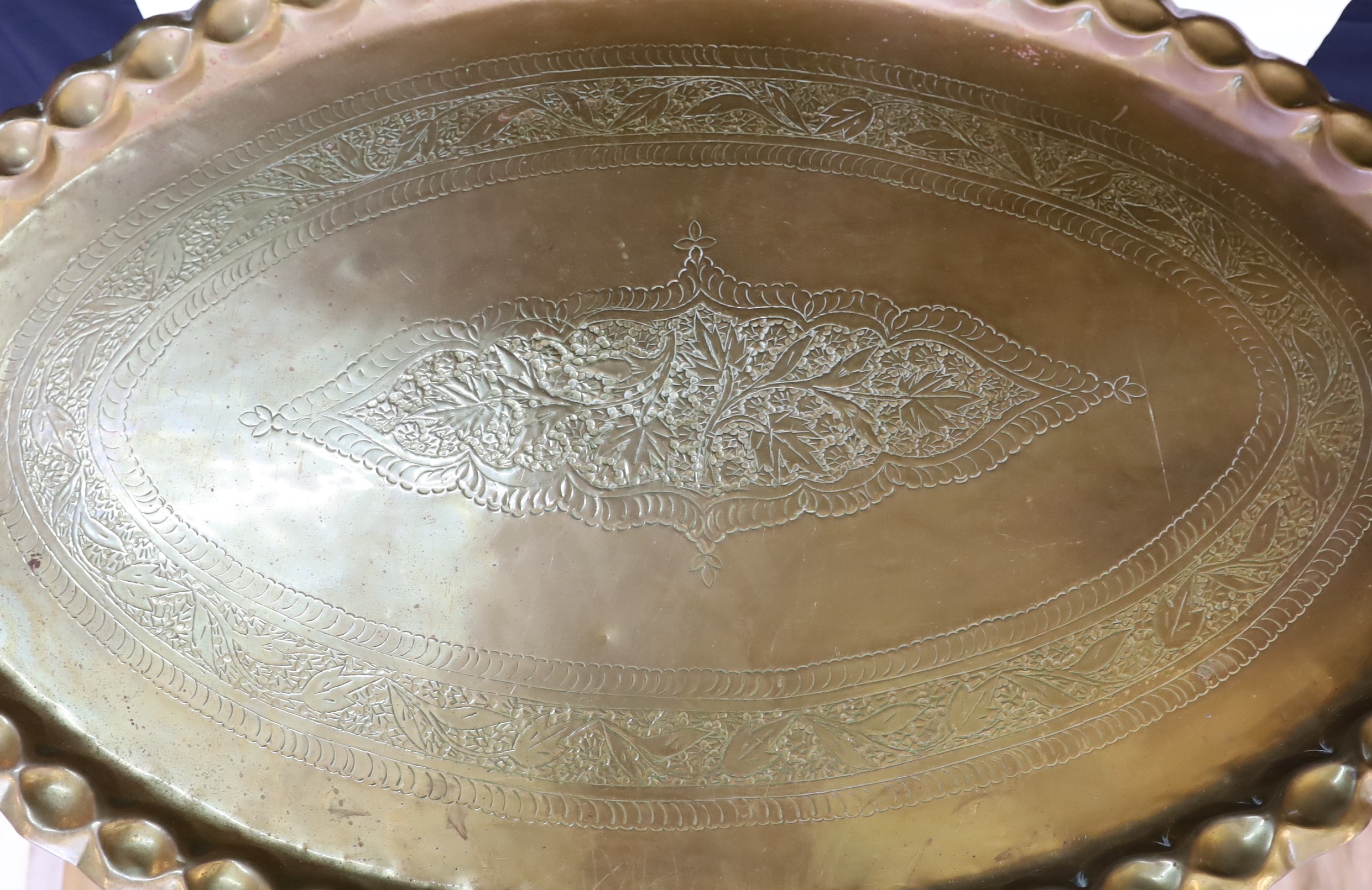 An unusually large early 20th century Indian brass oval tray top table with folding wooden underframe, 100 x 65cm. height 55cm